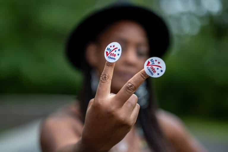 woman holds up 2 fingers, each with a VOTE sticker