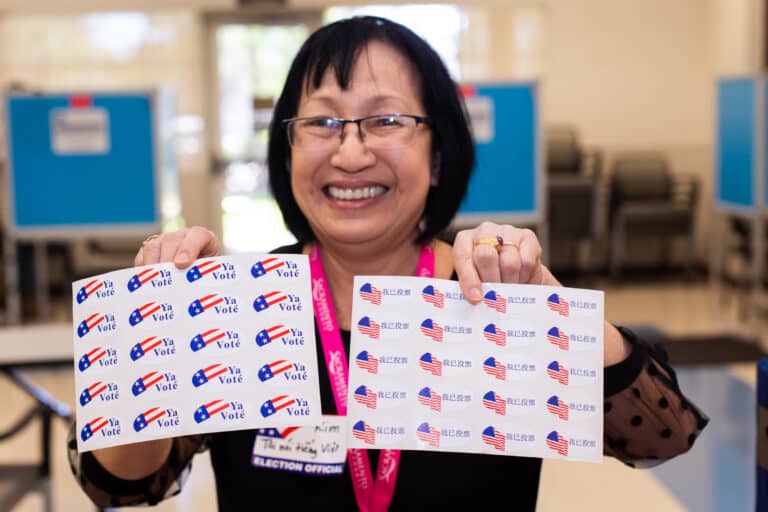 poll worker holding up "I Voted" sticker sheets