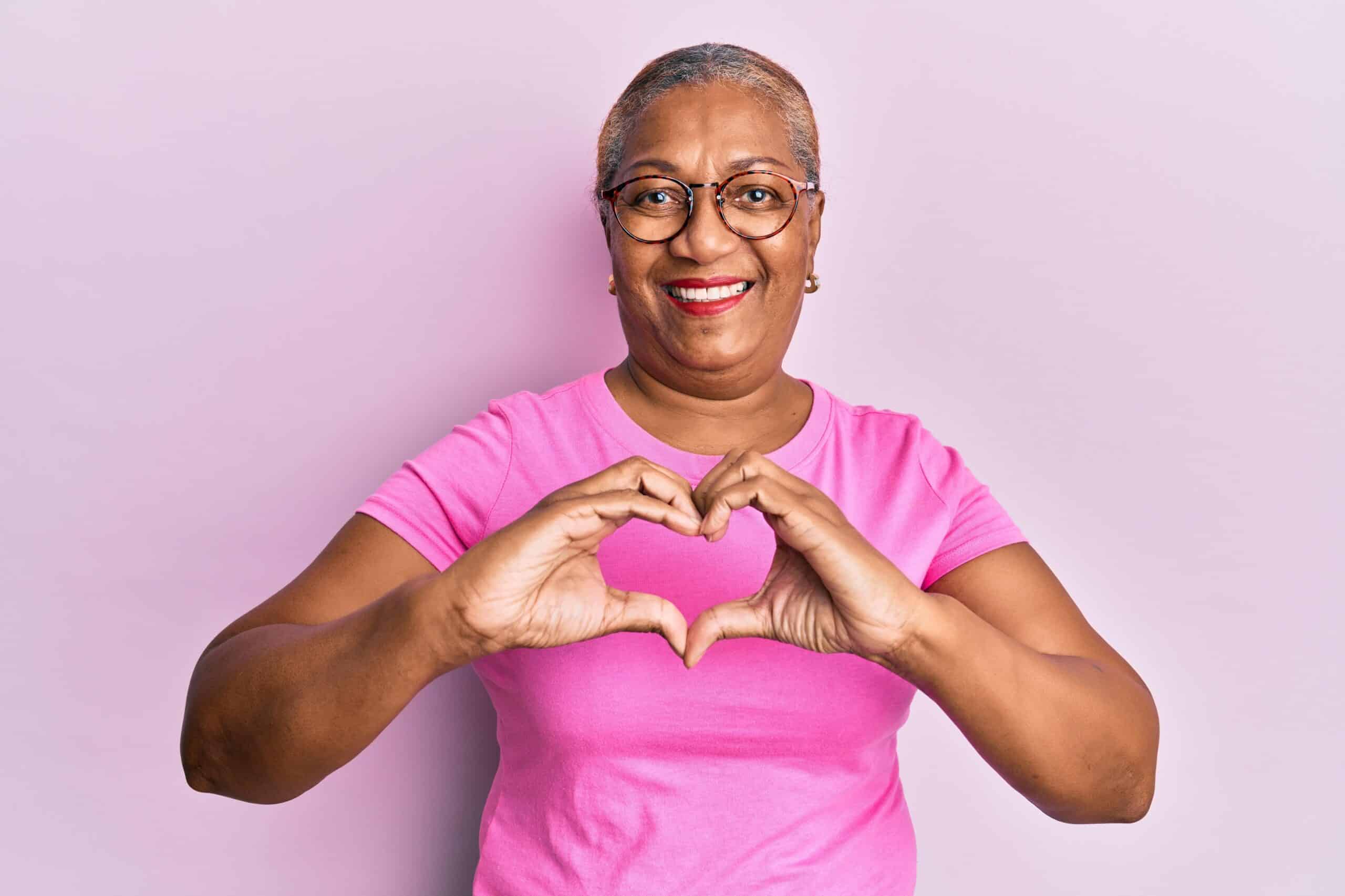 Senior African American woman wearing casual clothes and glasses smiling in love showing heart symbol and shape with hands.